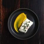 A dark round bowl with a swoosh of a saffron aioli and a sous vide halibut fillet.