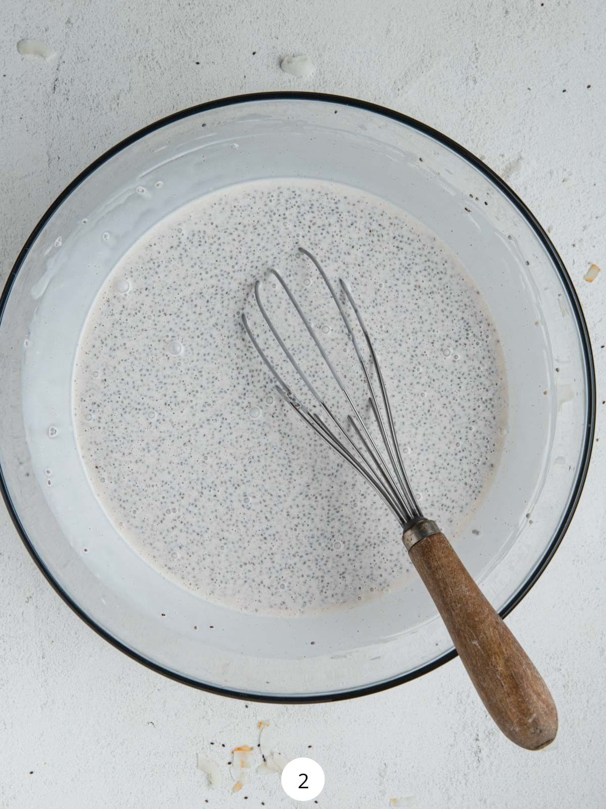 Coconut chia seed pudding mixture in a glass bowl with a whisk.