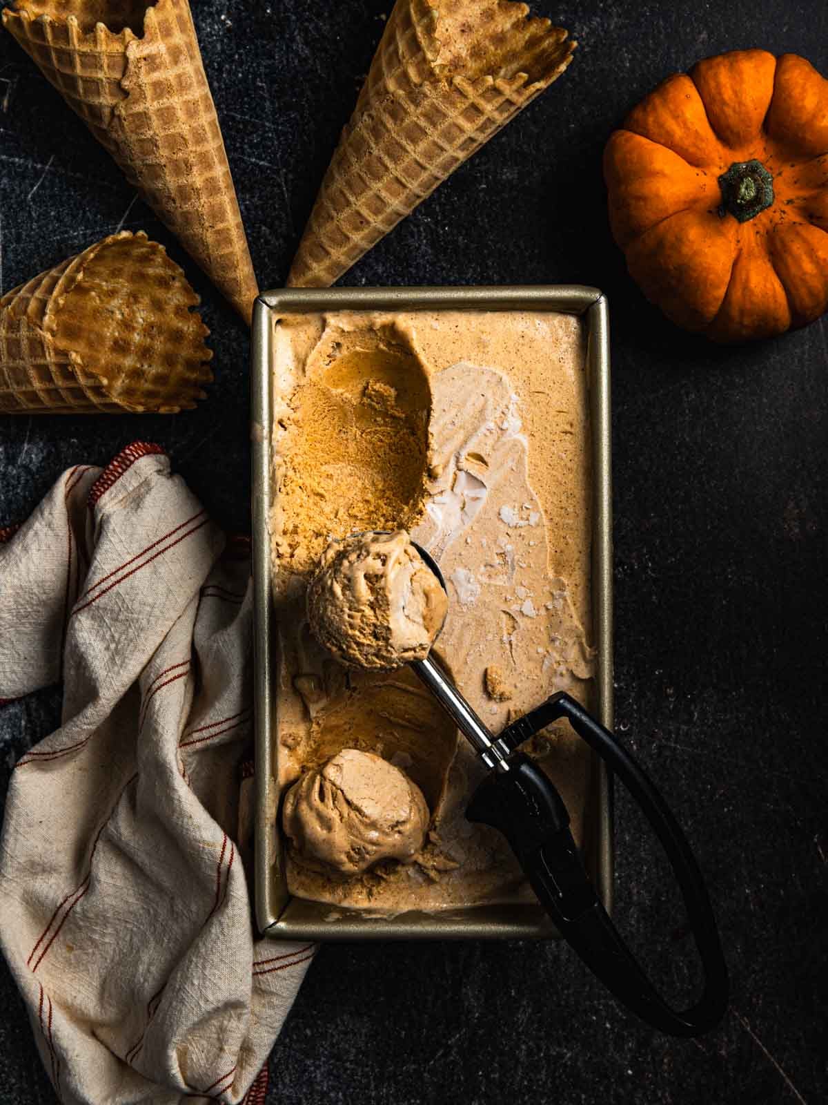 Pumpkin ice cream in a rectangular container with a metal scoop resting inside.