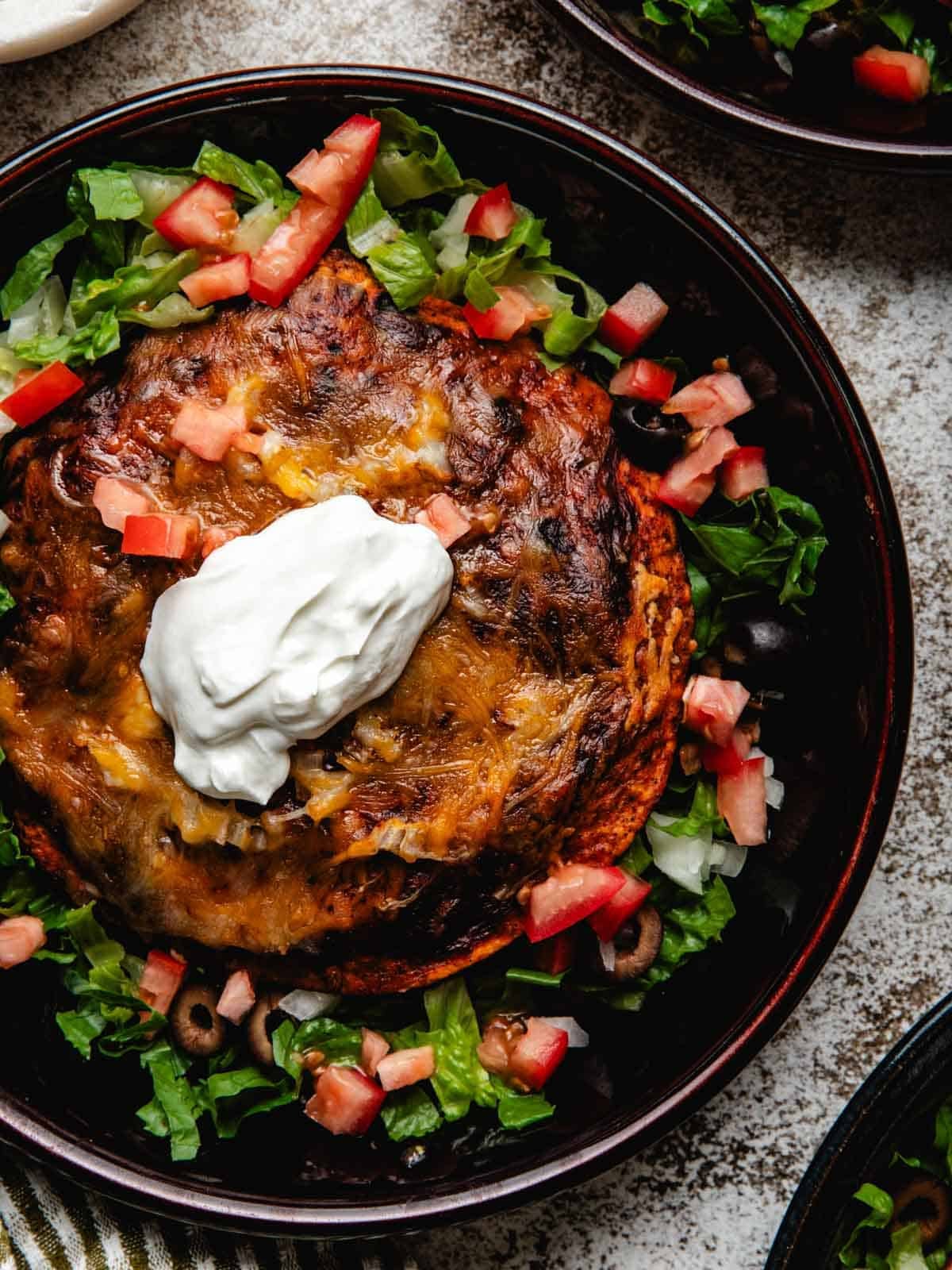 Three shallow bowls positioned next to each other with stacked beef enchiladas.