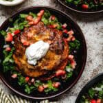 Three shallow bowls of stacked enchiladas garnished with lettuce, tomatoes, olives, and sour cream.