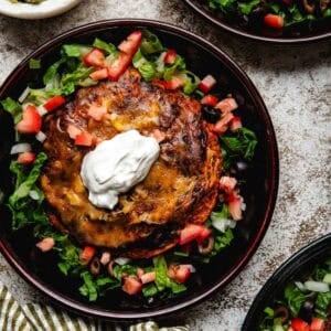 Three shallow bowls of stacked enchiladas garnished with lettuce, tomatoes, olives, and sour cream.