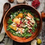 A large wooden bowl filled with an arugula pear salad.