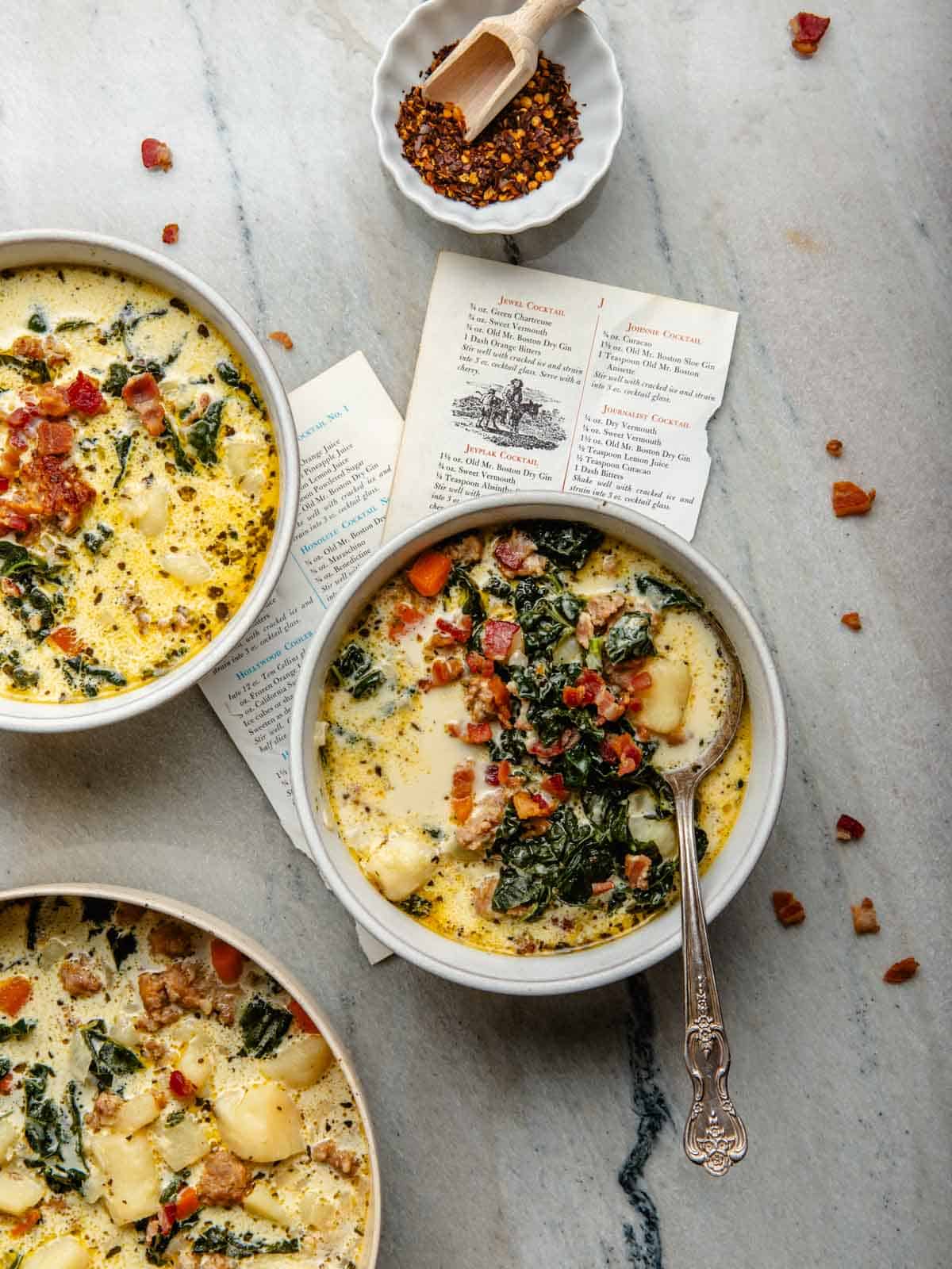 Three round soup bowls fill with a sausage, potato, and kale soup with a soup spoon inside one of the bowls.