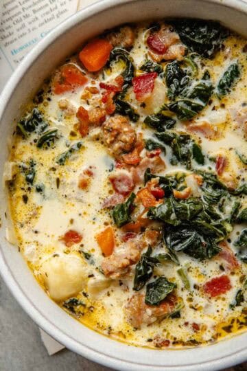 A round bowl filled with a sausage, potato, and kale soup.