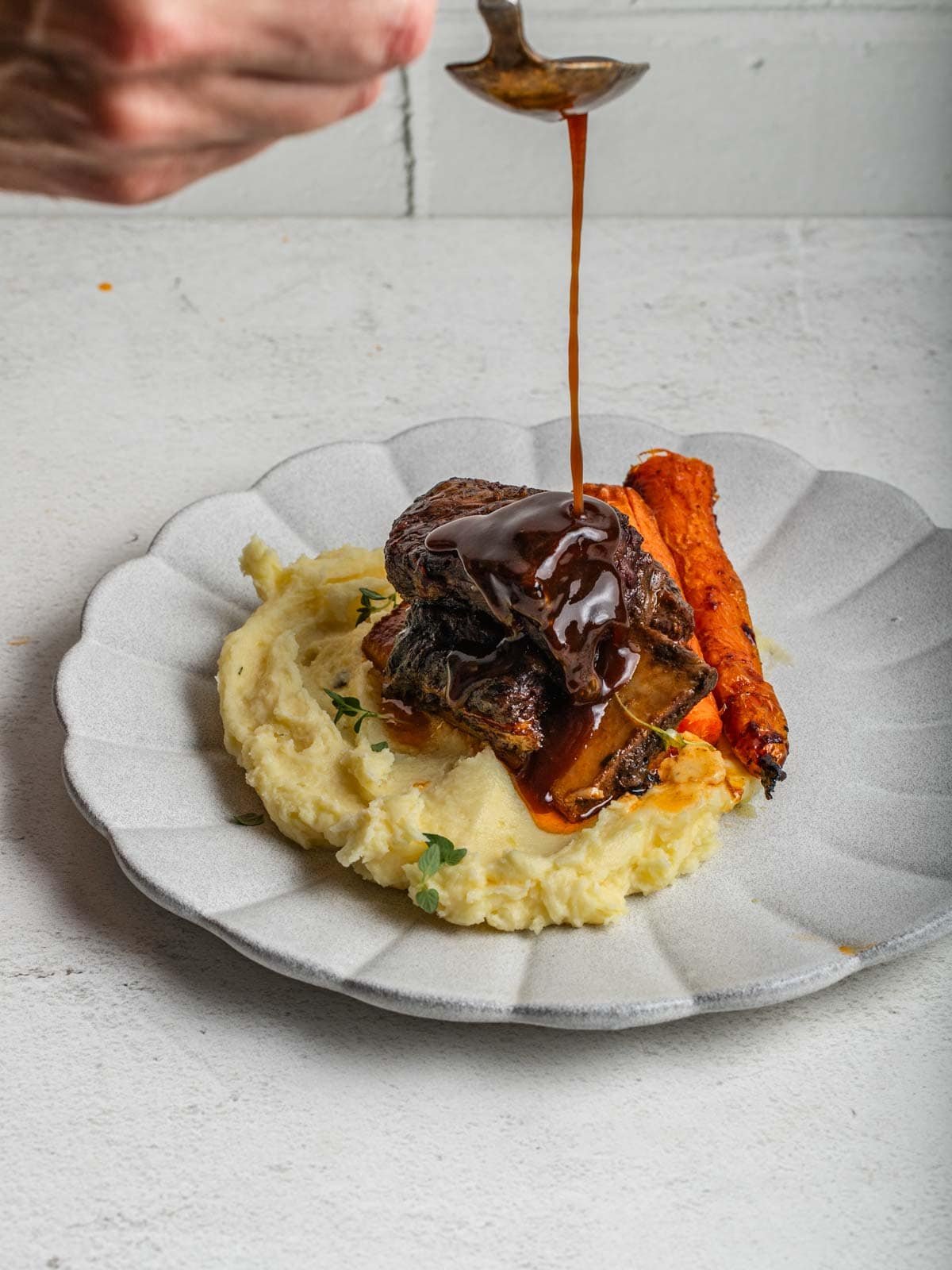 Drizzling a homemade Demi Glace sauce over top of a braised short rib.