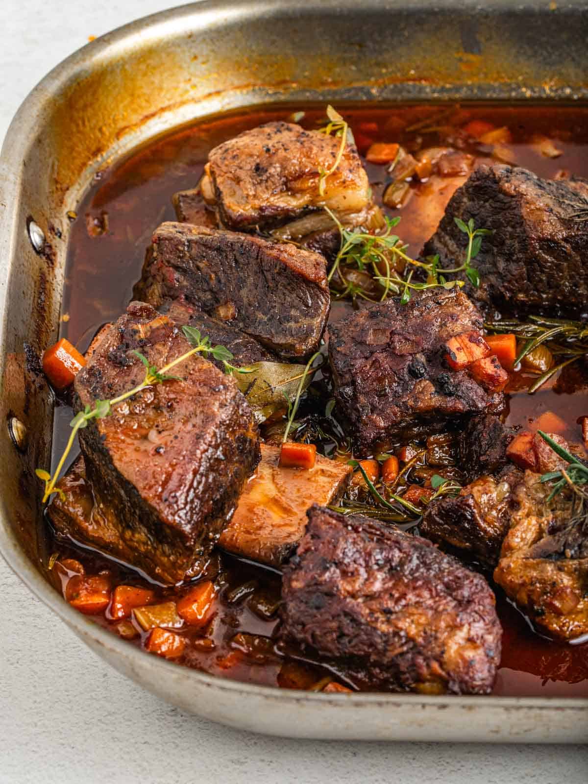 A stainless-steel roasting pan filled with braised short ribs.