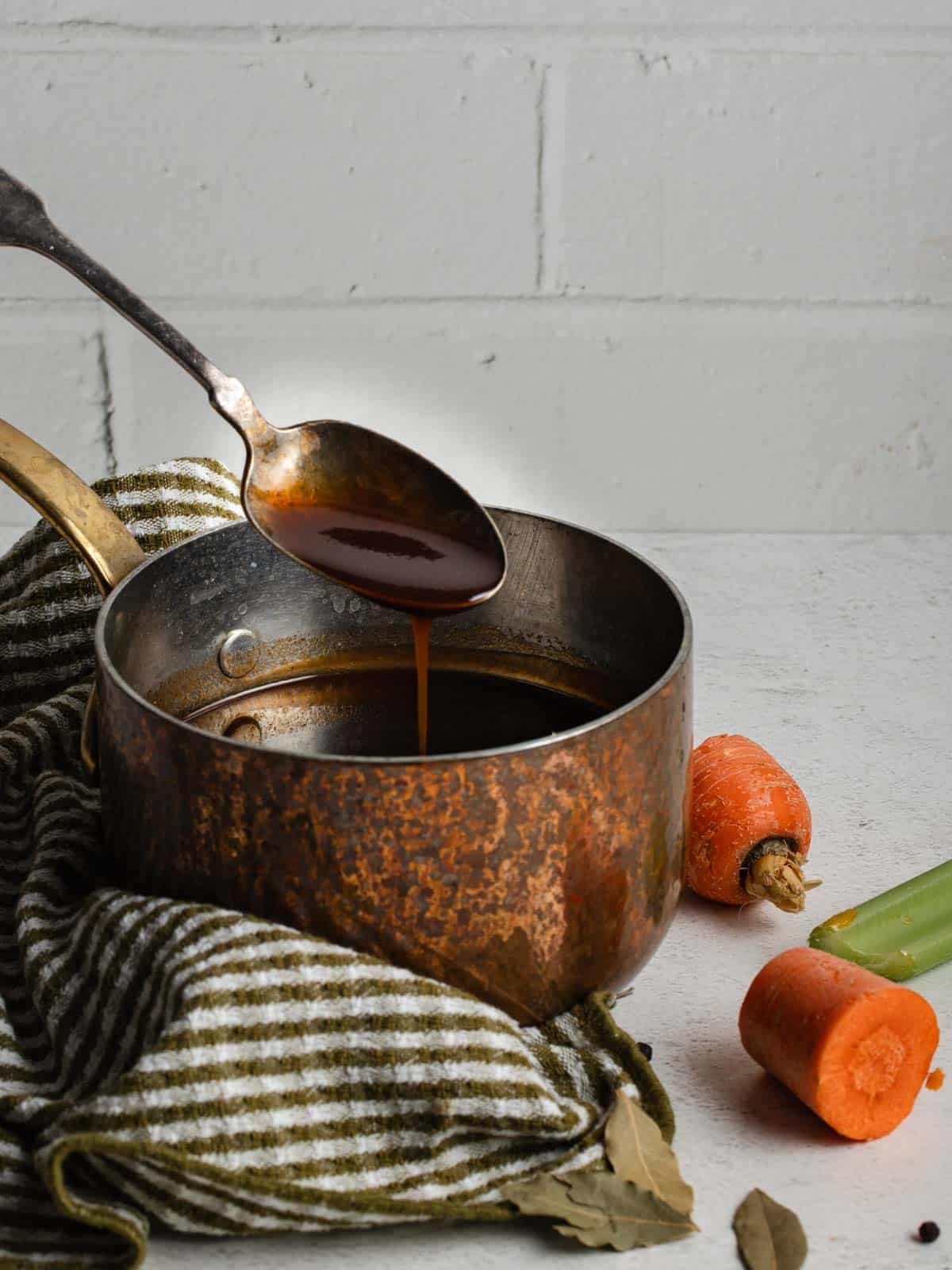 A spoon coated with demi-glace sauce dripping over a small saucepan.