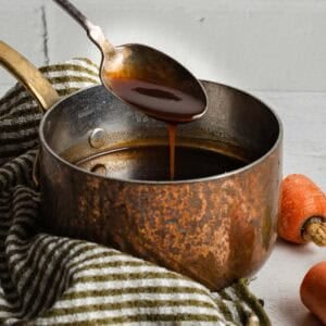 A spoon coated with a demi-glace sauce dripping over a small sauce pan.