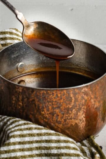 A spoon coated with a demi-glace sauce dripping over a small sauce pan.