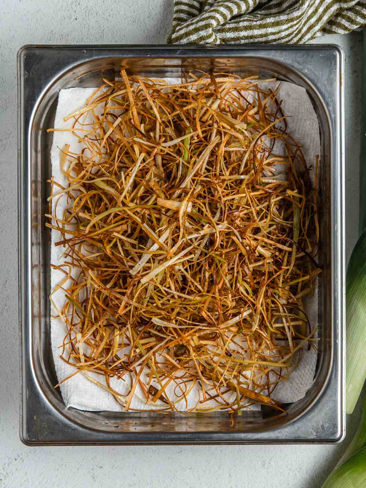 A paper towel lined pan with crispy fried leeks.