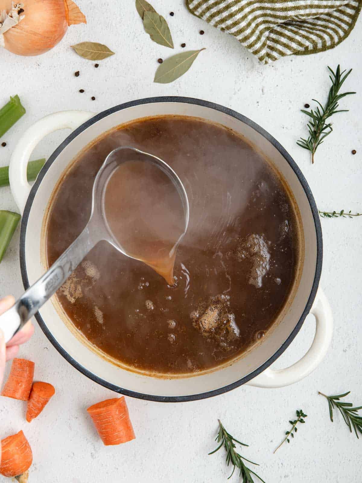 A dutch oven filled with hot veal stock with a ladle.