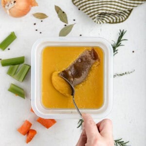A spoon removing the fat cap off the top of veal stock.