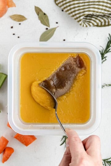 A spoon removing the fat cap off the top of veal stock.