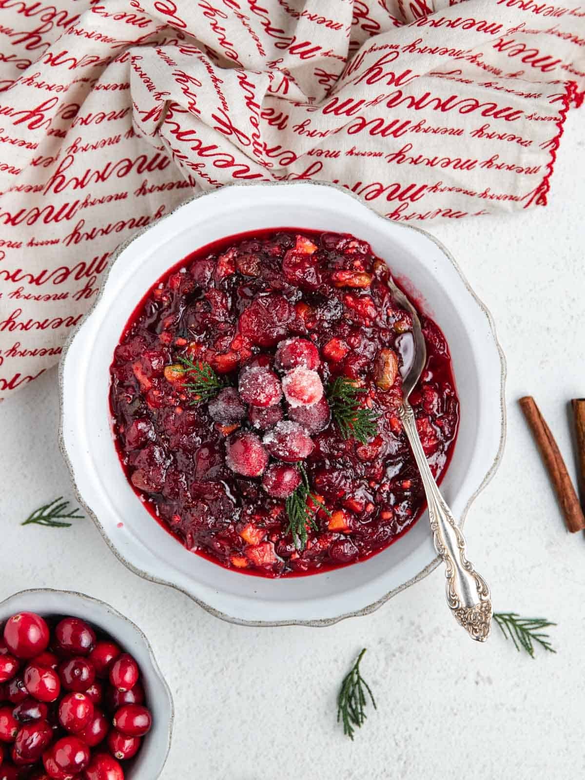 Cranberry chutney inside of a flutted bowl garnished with sugared cranberries and fresh rosemary.