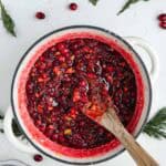 Finished cranberry chutney inside of a white Dutch oven with a wooden spoon.