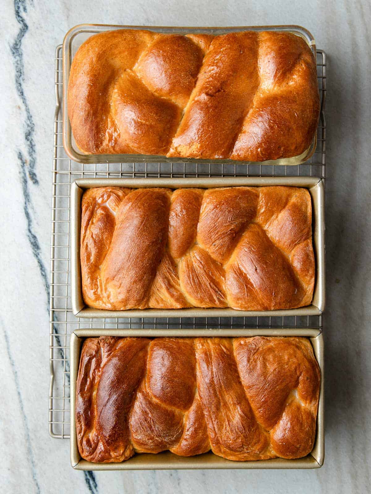 Three loaf pans of Nisu bread resting on a wire cooling rack.