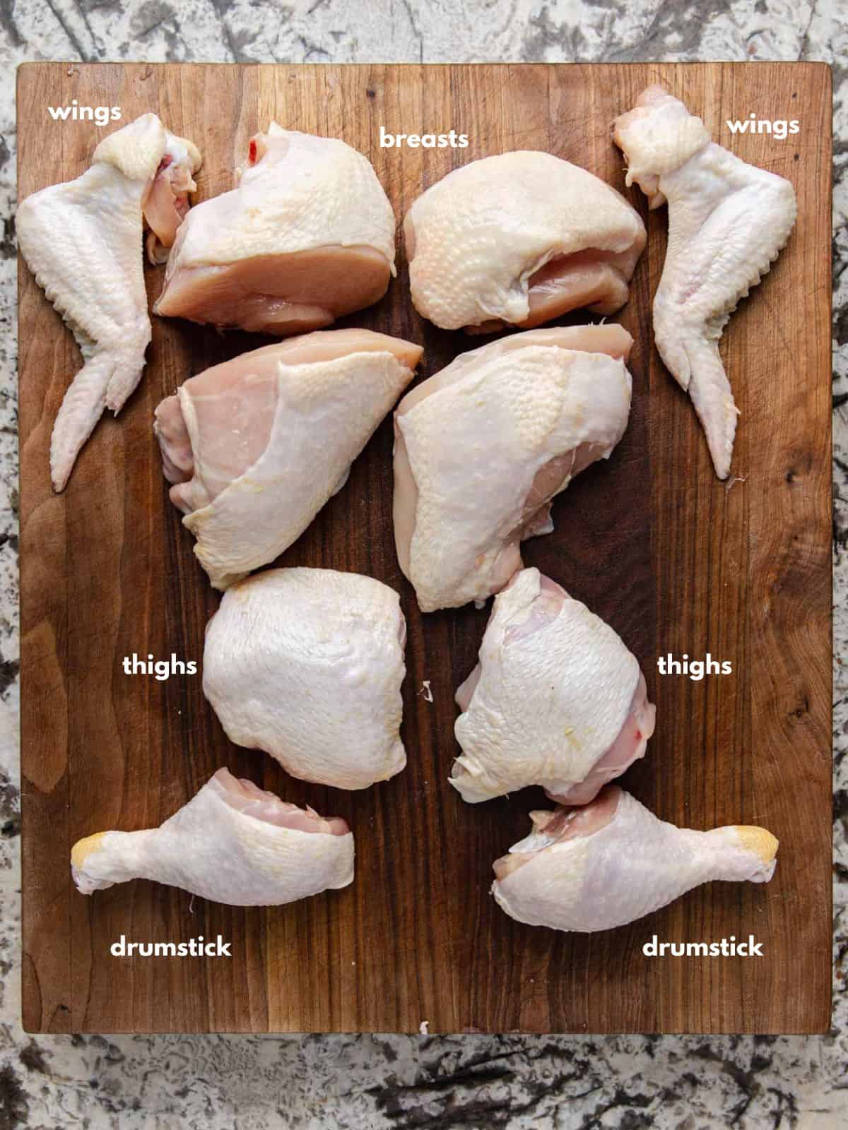 Chicken wings, breasts, thighs, and drumsticks on a wooden cutting board.