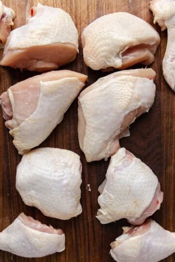Chicken cut up into 10-pieces on a wooden cutting board.