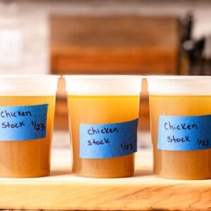 Chicken stock in quart containers in a row on a wooden cutting board.