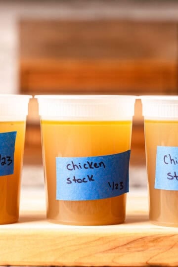 Chicken stock in quart containers in a row on a wooden cutting board.