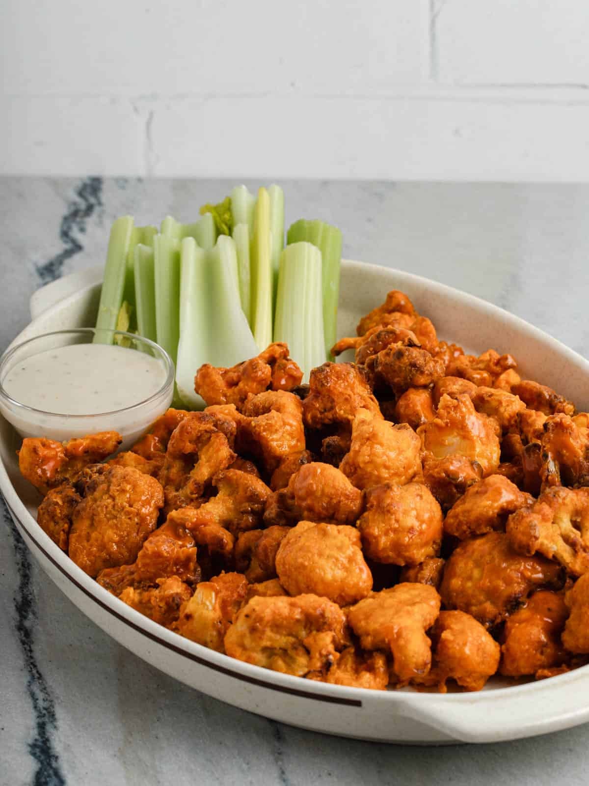 Buffalo cauliflower on a oval platter with blue cheese dressing and celery sticks.