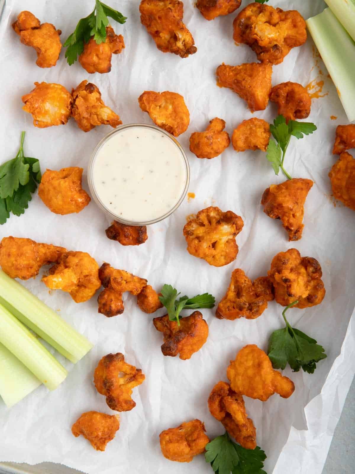 Buffalo cauliflower on a parchment-lined sheet pan with celery sticks and blue cheese dressing.