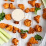 Buffalo cauliflower on a parchment-lined sheet pan with celery sticks and blue cheese dressing.