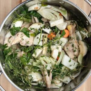 Chicken bones, vegetables, herbs, and cold water in a stainless steel stock pot.