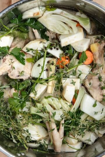 Chicken bones, vegetables, herbs, and cold water in a stainless steel stock pot.
