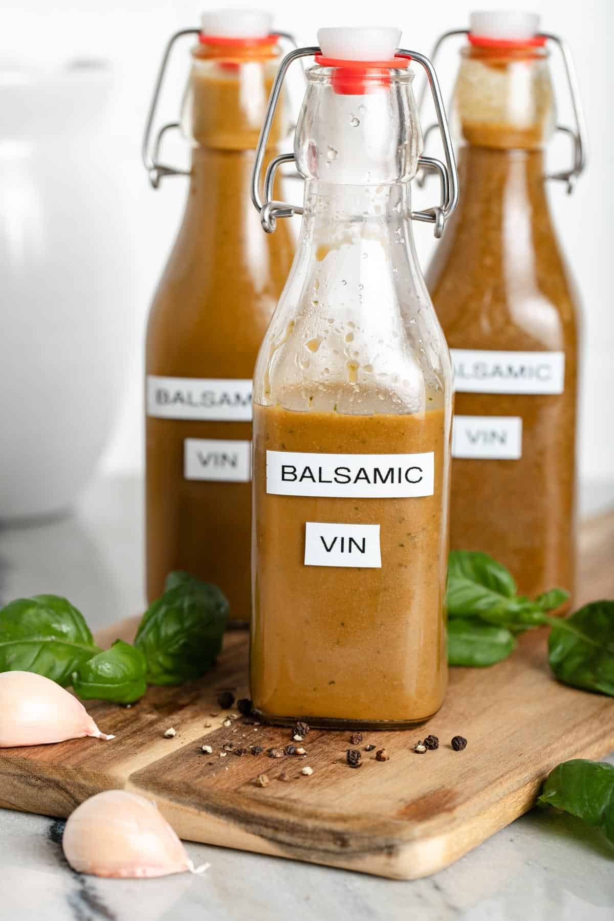 Three glass bottles of balsamic vinaigrette sitting on a wooden cutting board.