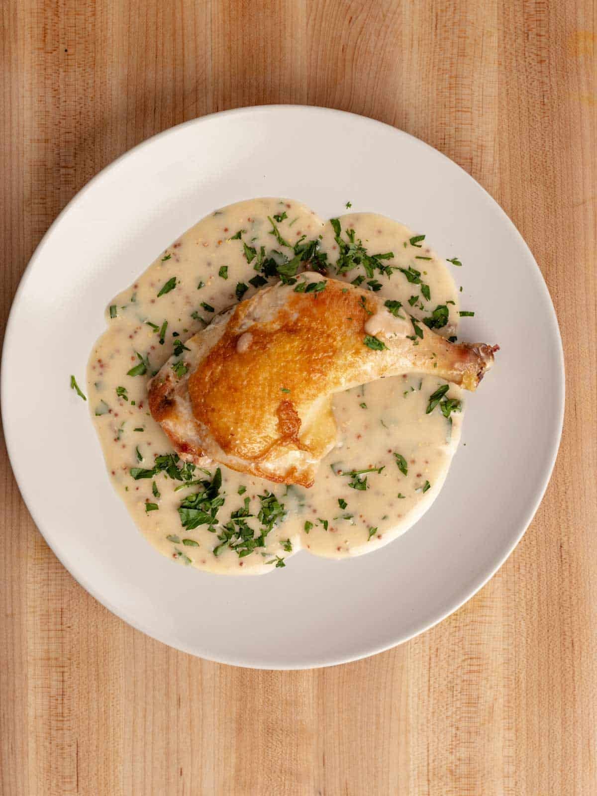 Crispy chicken leg with a mustard velouté presented on a round white plate.