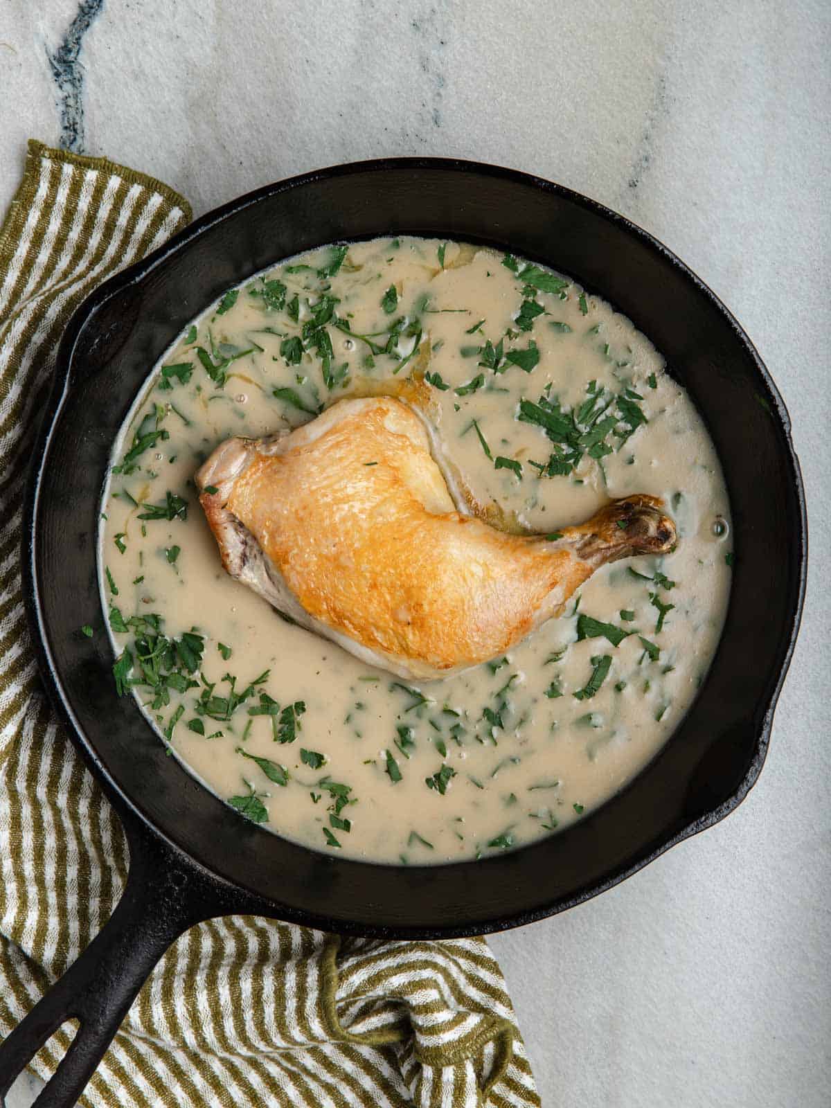 Crispy chicken leg in a cast iron pan with velouté sauce.