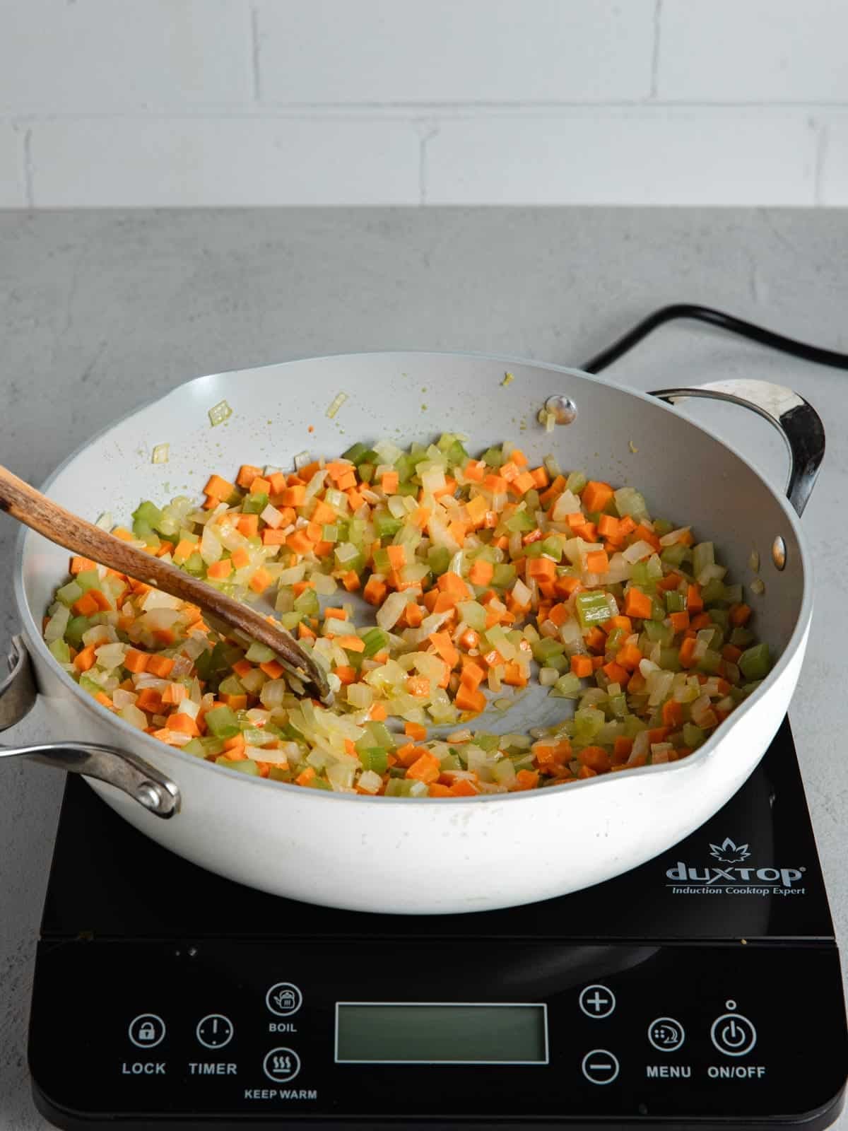 Sweating mirepoix in a large pan with a wooden spoon.