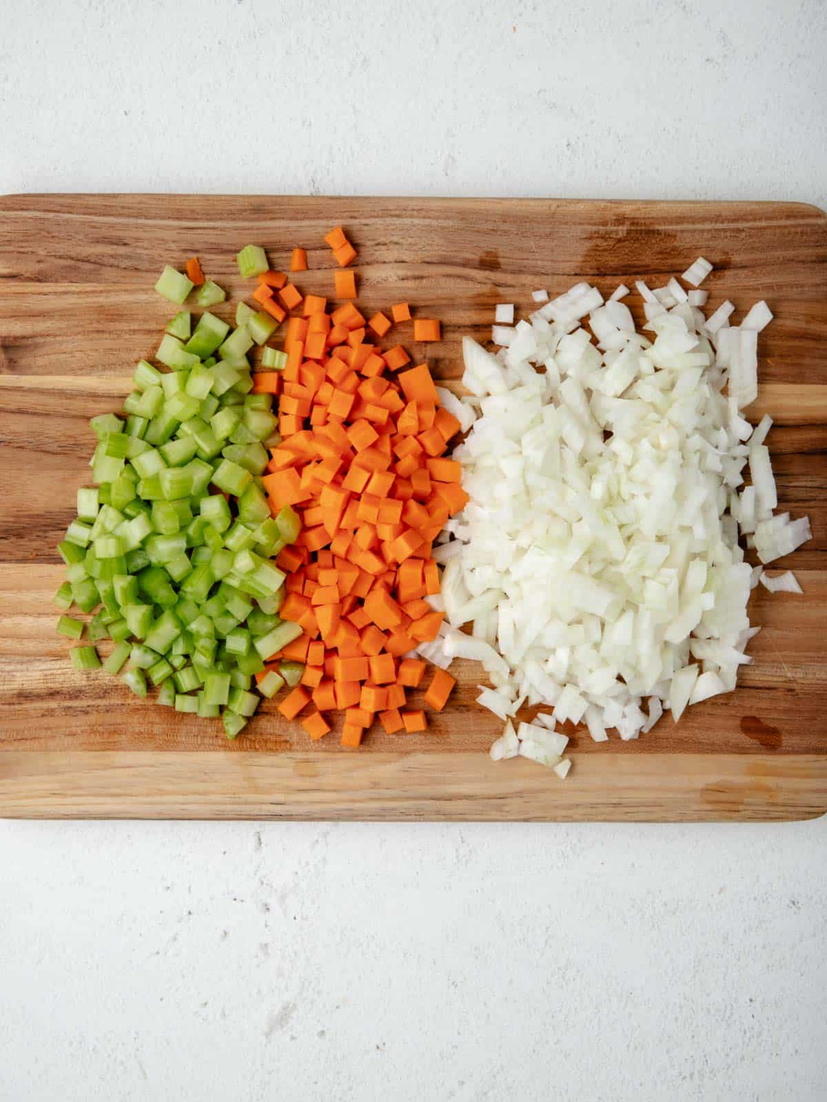Diced onions, celery, and carrots on a wooden cutting board.