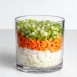 Dice onions, carrots, and celery layered in a large glass jar.