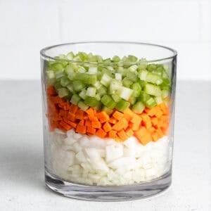 Dice onions, carrots, and celery layered in a large glass jar.