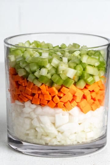 Dice onions, carrots, and celery layered in a large glass jar.