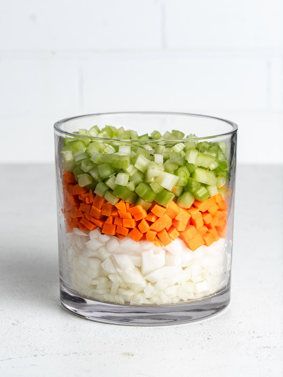 A glass jar with onions, carrots, and celery layered.