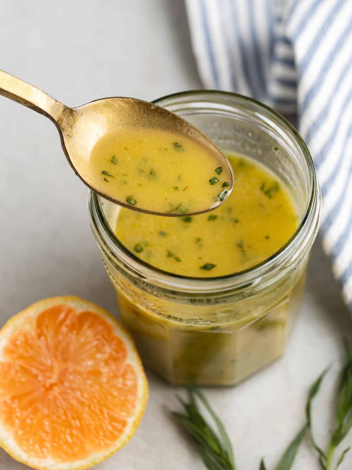 Lemon-tarragon dressing in a glass jar with a gold spoon.