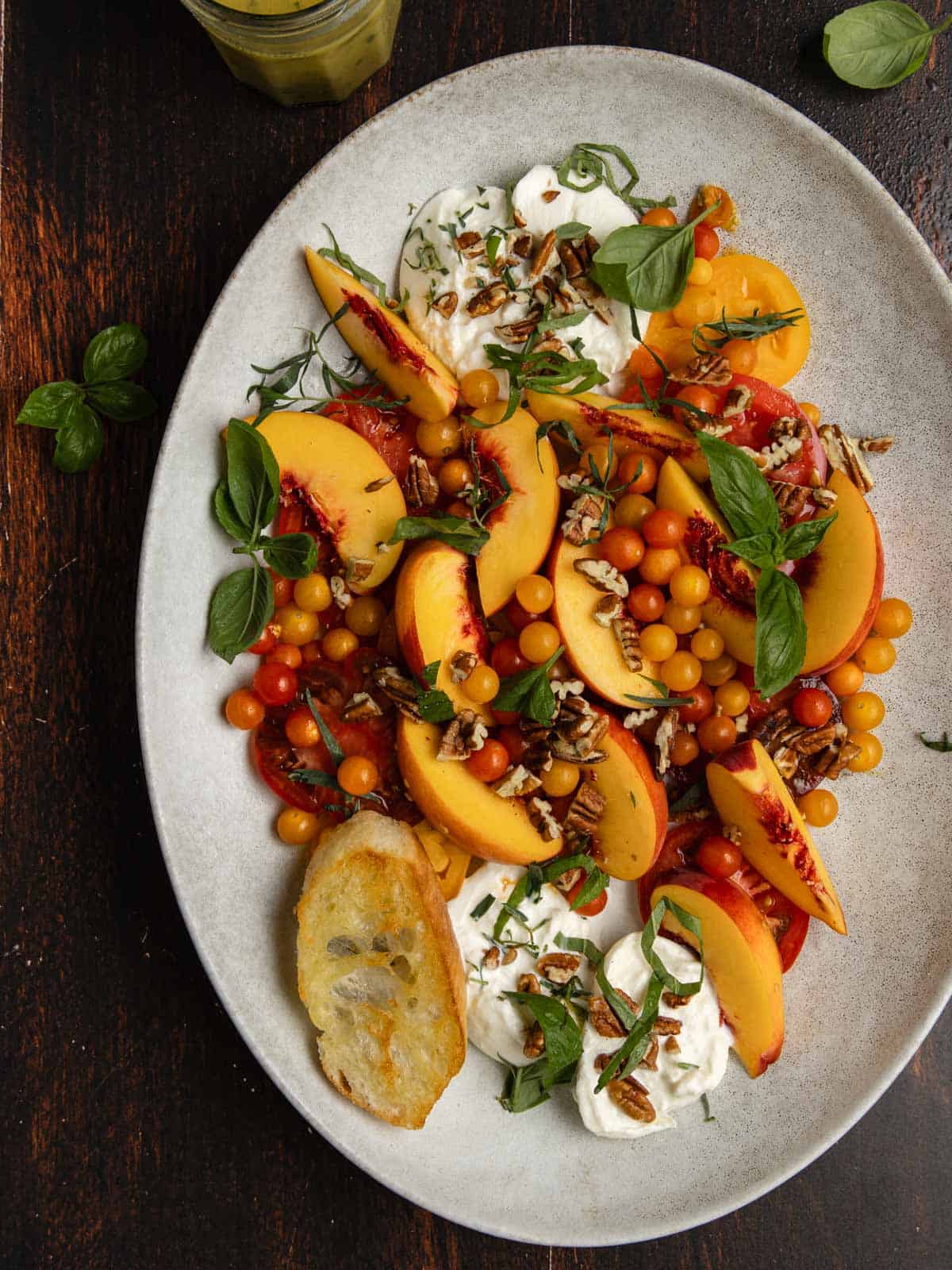 Tomato, peach, burrata salad on an oval serving platter with fresh basil.