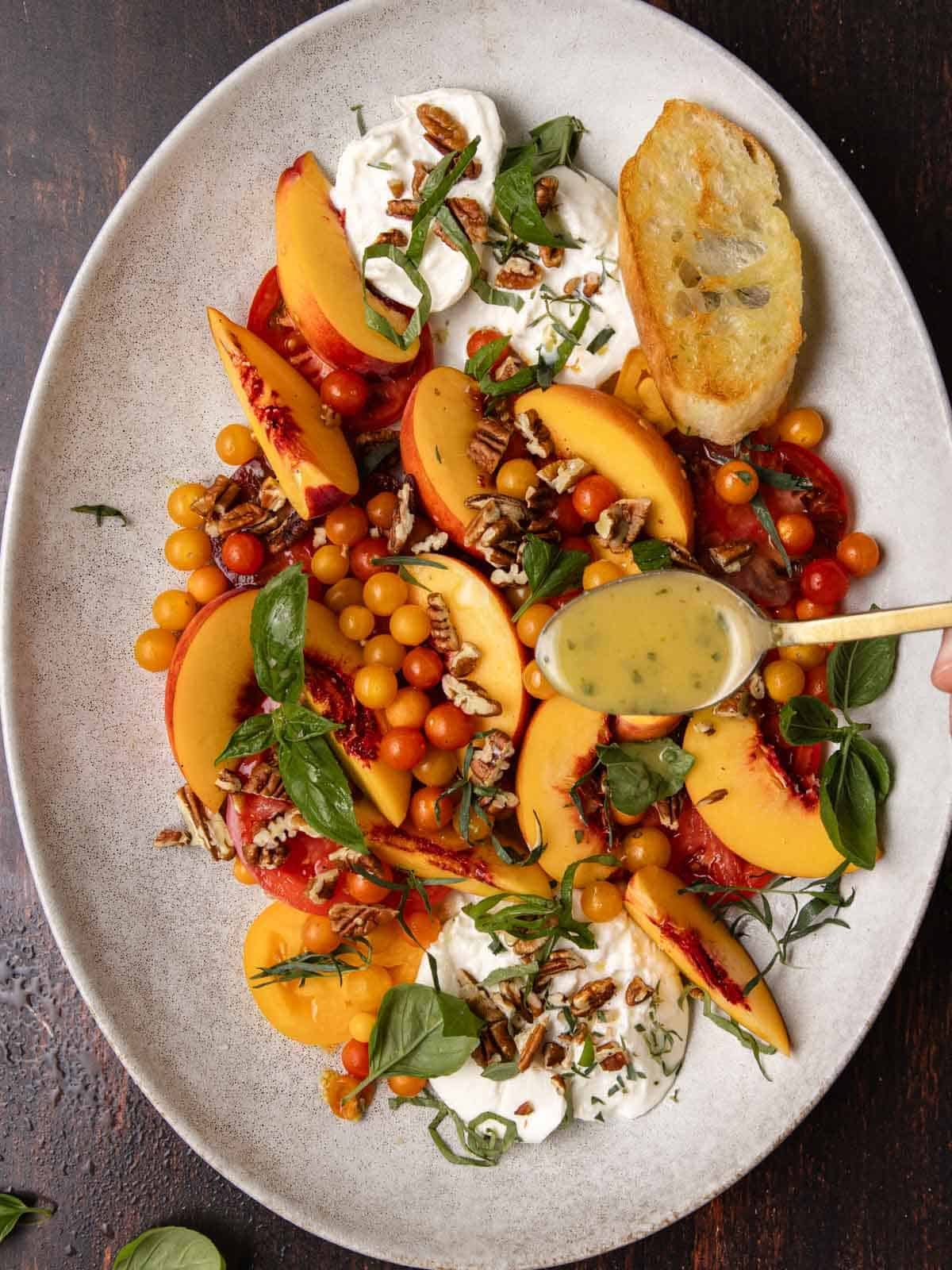 Using a golden spoon to drizzle lemon-tarragon dressing over fresh tomatoes and peaches.