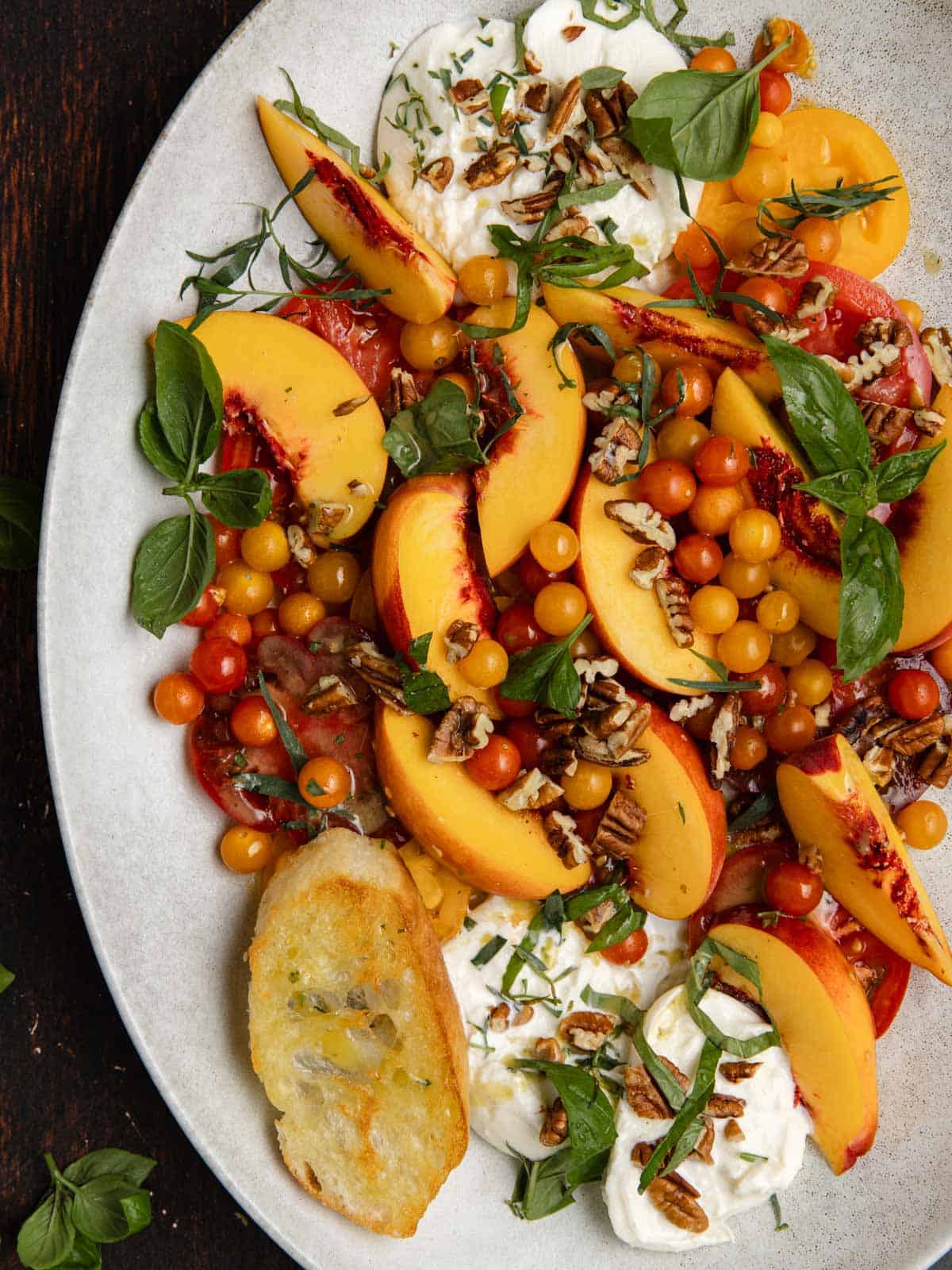 Tomato, peach, burrata salad on an oval serving platter with fresh basil.