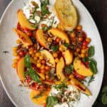 Tomato, peach, burrata salad on an oval serving platter with fresh basil.