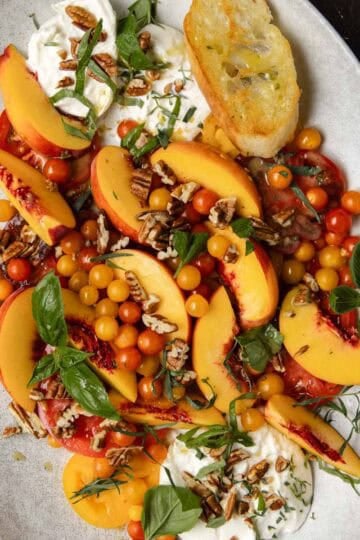 Tomato, peach, burrata salad on an oval serving platter with fresh basil.