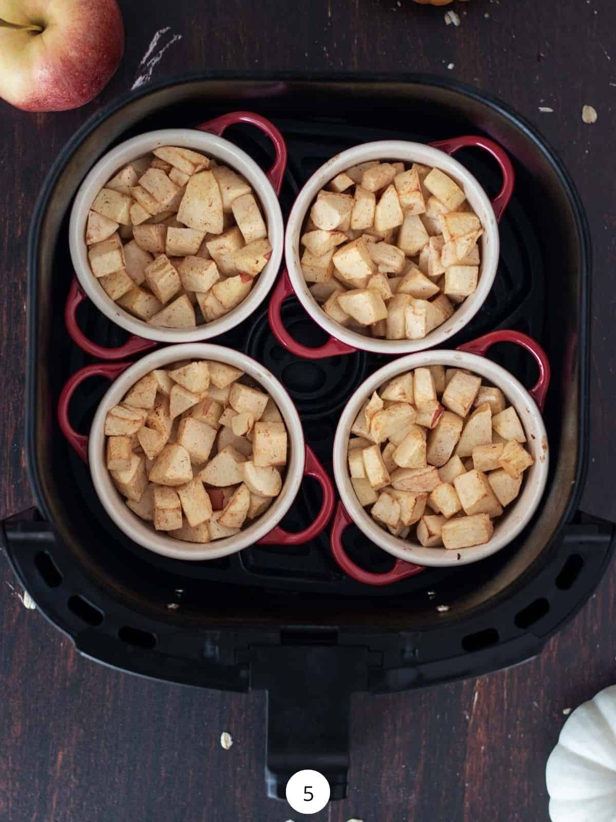 Four cocottes filled with cooked apples inside of an air fryer basket.