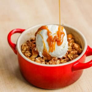 Drizzling caramel sauce over apple crispy and a scoop of vanilla ice cream.