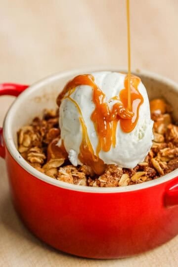 Drizzling caramel sauce over apple crispy and a scoop of vanilla ice cream.