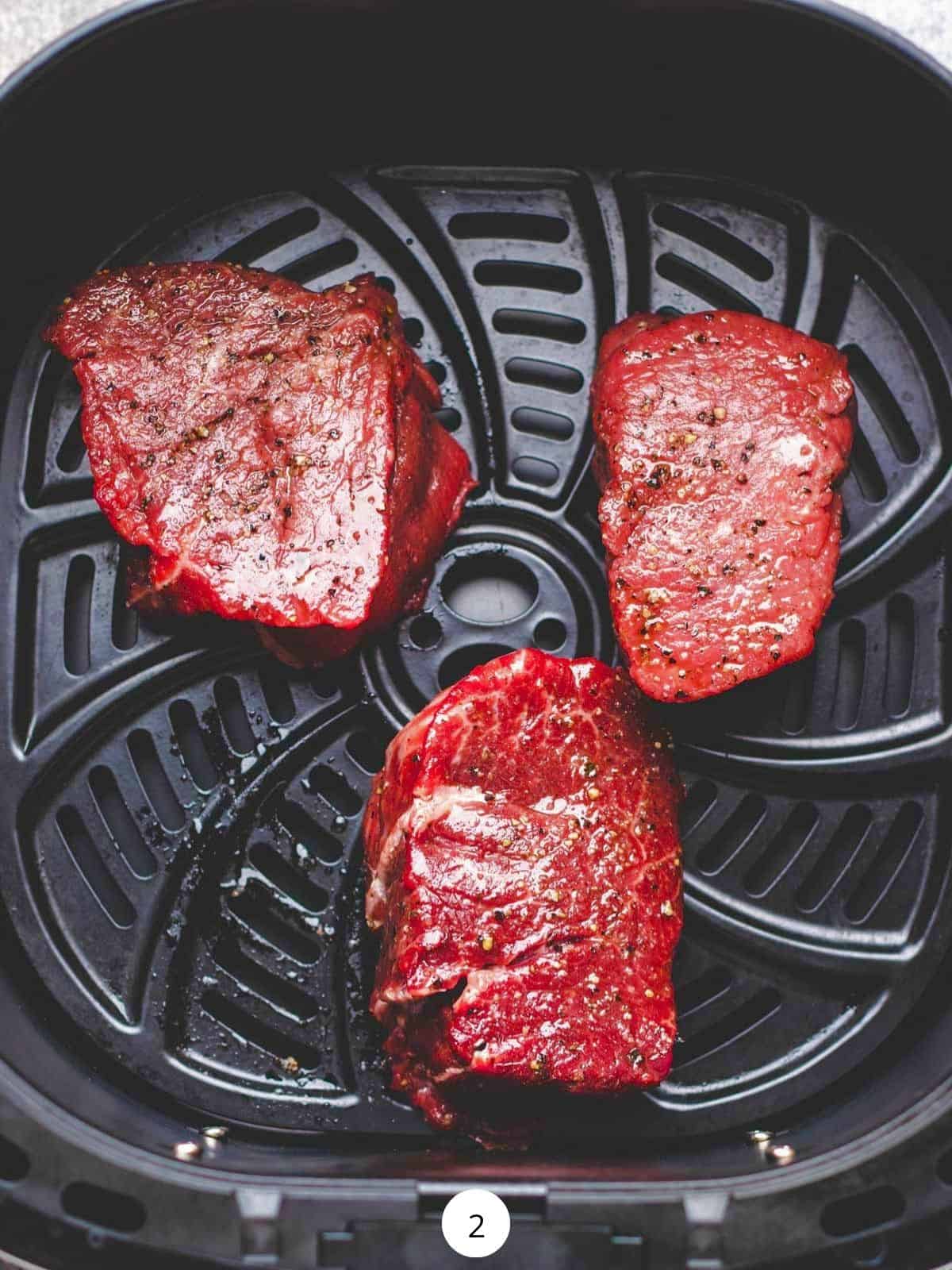 Three raw filet mignon steaks inside the air fryer basket.
