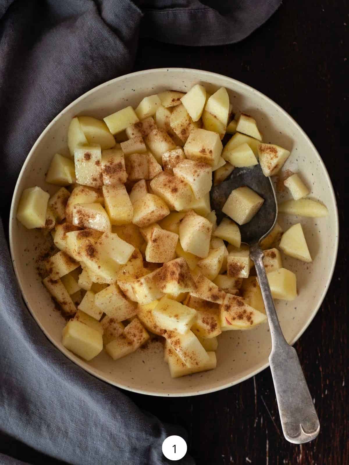 Mixing diced apples with cinnamon in a round bowl with a spoon.
